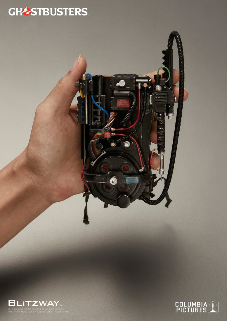 A hand holding the 1/6 scale proton pack accessory from Blitzway’s Ghostbusters action figure, showcasing intricate wiring, painted components, and mechanical detailing on the back side.